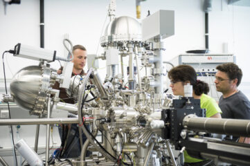 Three researchers - one female and two male - constructing a complex machinery with many silver tubes in a laboratory